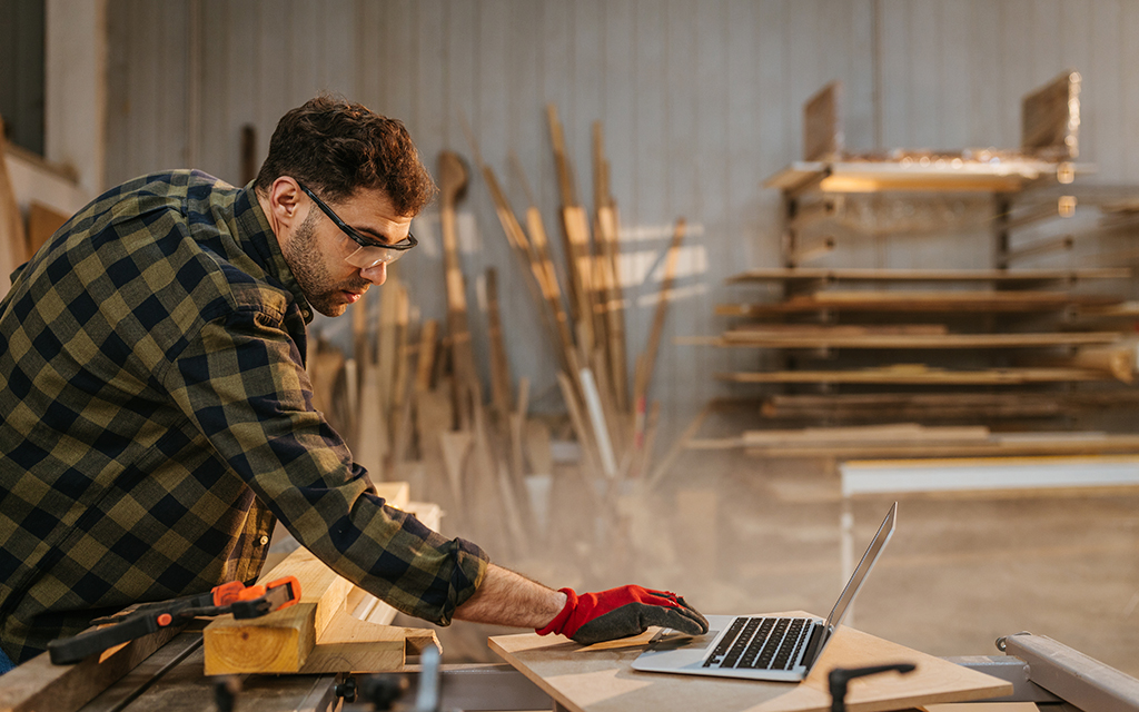 Young adult carpenter in a workshop with a laptop