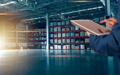 Modern warehouse with shelves full of products and a person holding a tablet for inventory management